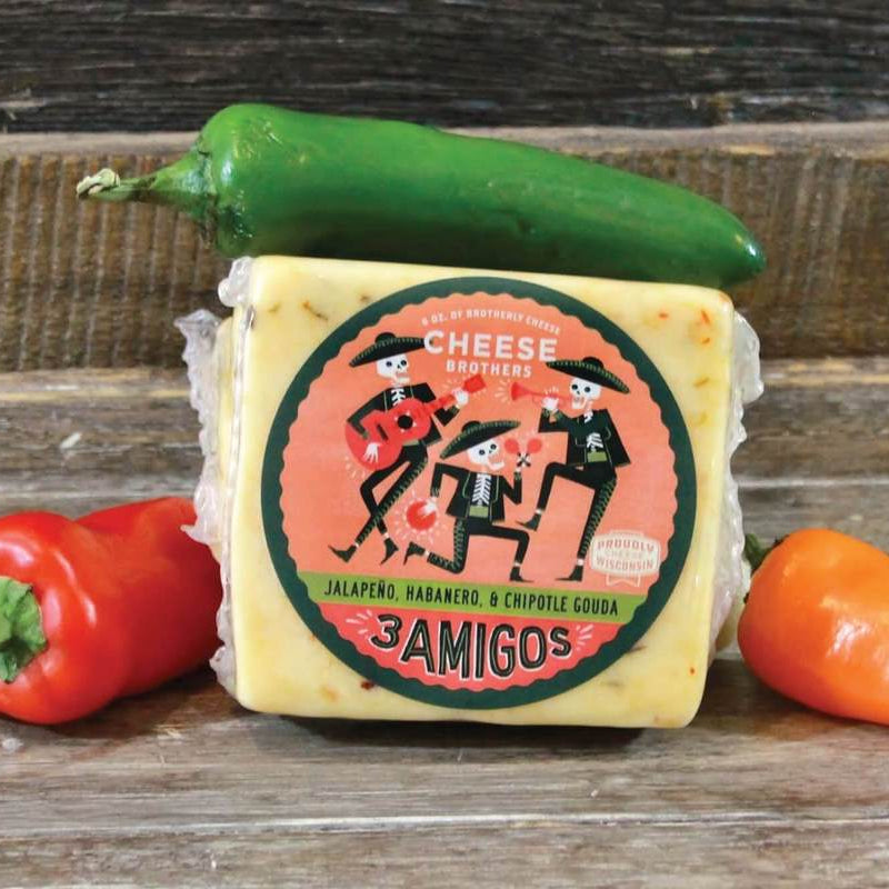 Block of cheese with a 'Amigos' label surrounded by peppers on a wooden surface