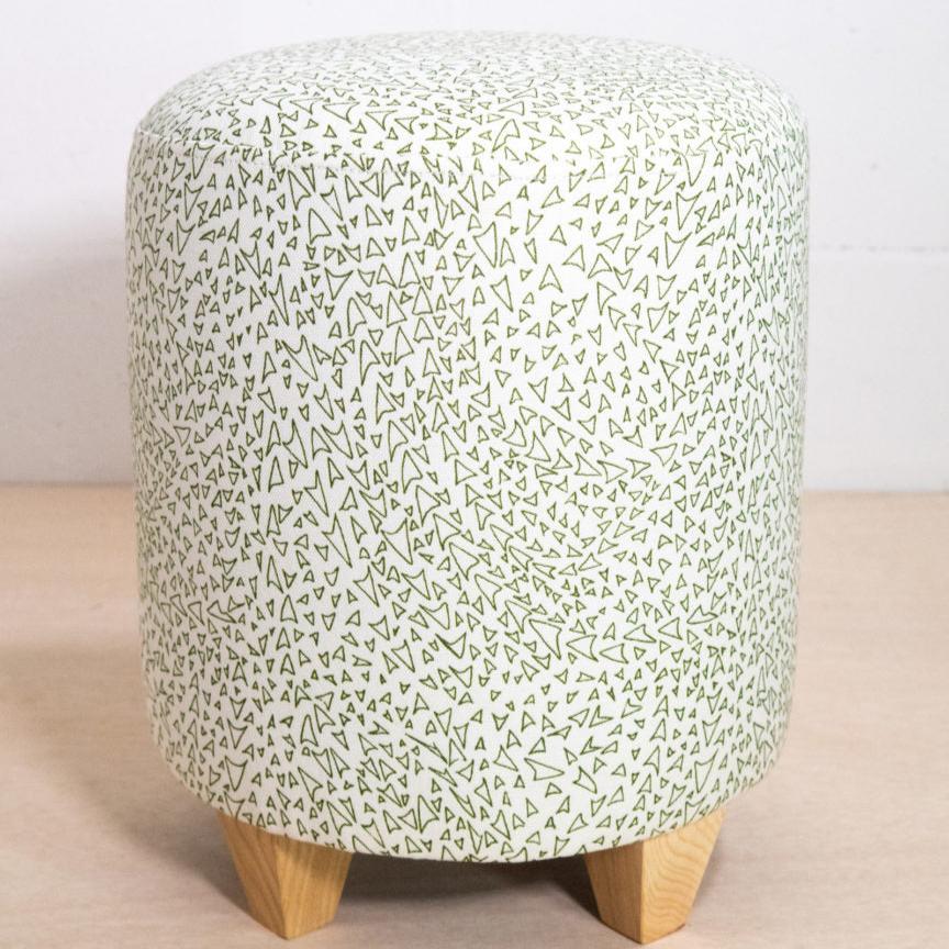 A small round ottoman with a geometric pattern in green and white upholstery, supported by a wooden frame.