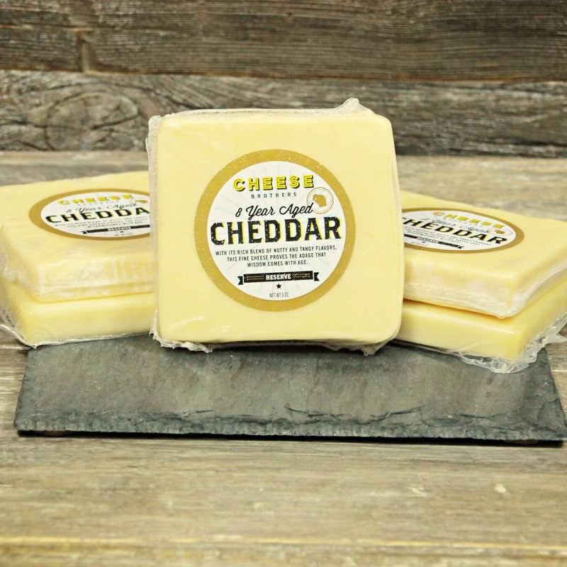 Three blocks of cheddar cheese with labels on a wooden surface