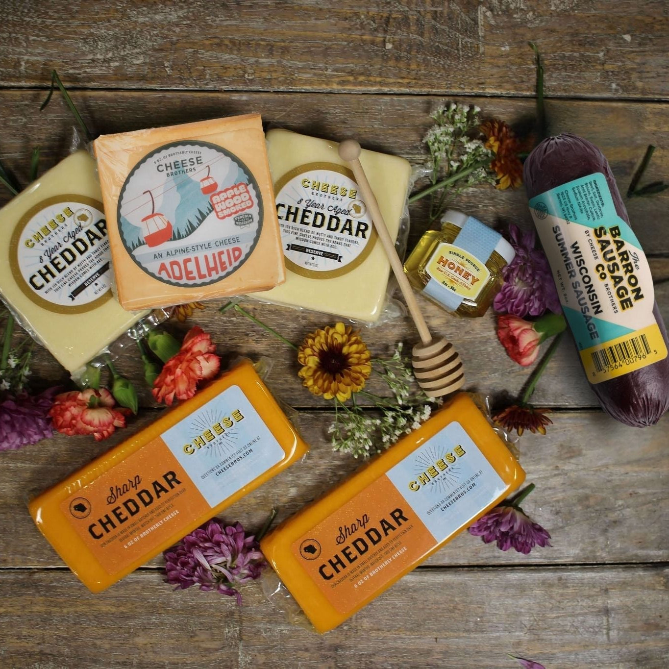 Various types of cheddar cheese and honey on a wooden surface with flowers.