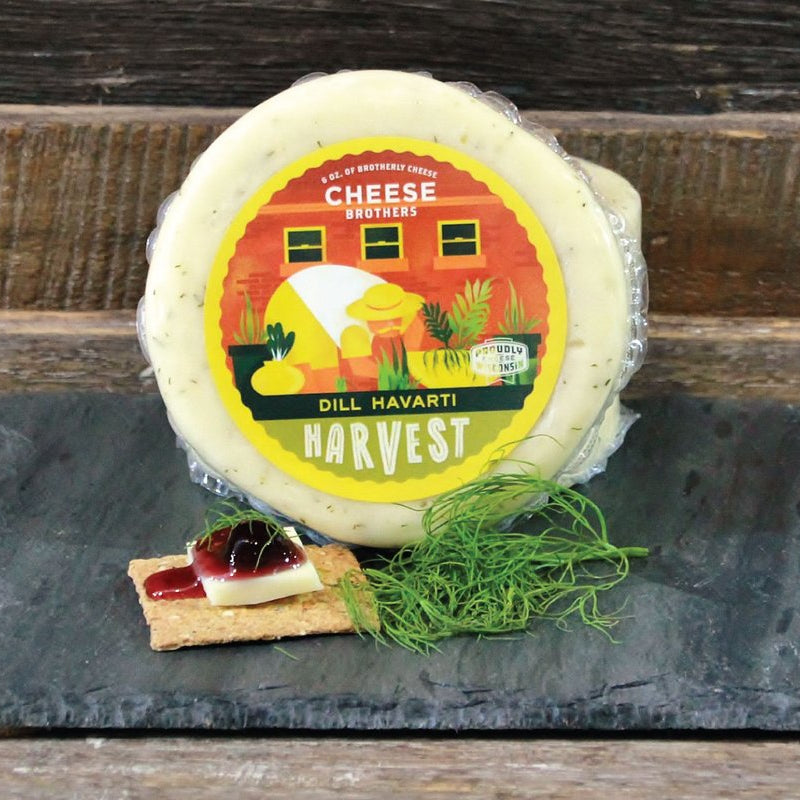 Dill Havarti cheese wheel with a decorative label on a slate board with a wooden background