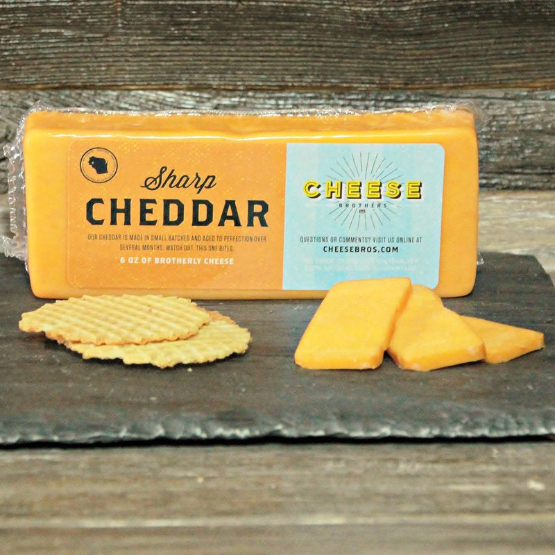 Block of Sharp Cheddar cheese with crackers on a slate board against a wooden background