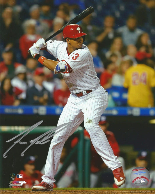 Baseball player in a white uniform with red helmet swinging a bat, with a crowd in the background.