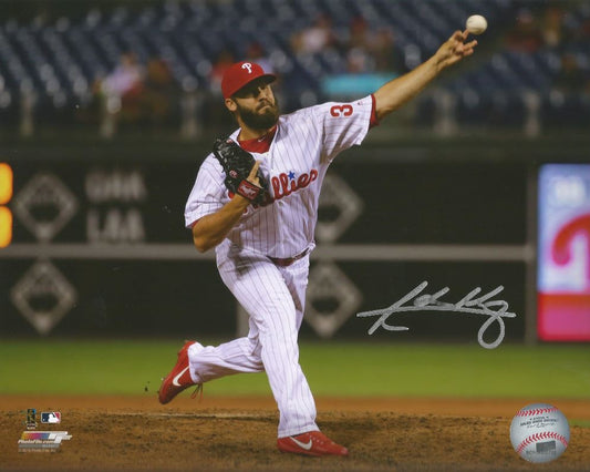 Baseball player in a white uniform with red accents, pitching on a baseball field.