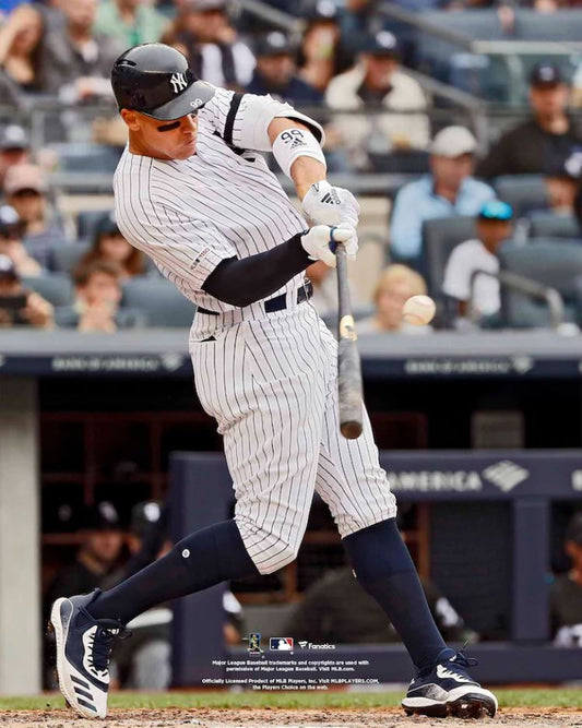 Baseball player in pinstripe uniform swinging a bat on a baseball field with spectators in the stands.