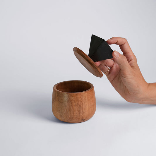 A round wooden jewel box with a lid, being opened by a person using a black onyx gemstone handle.