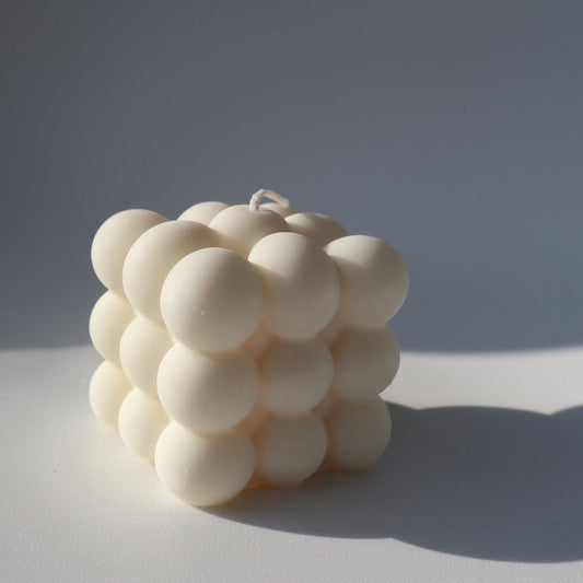 A white, spherical candle with a textured surface, placed on a white background.